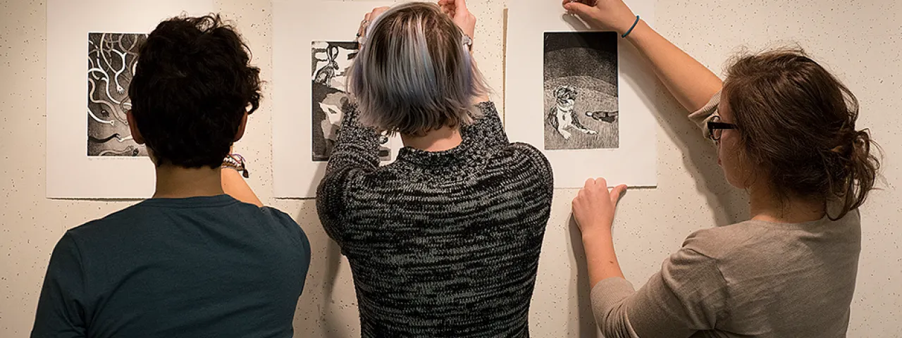 Three students hanging art on a gallery wall