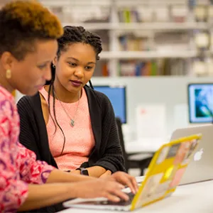 A student working on a laptop with a librarian