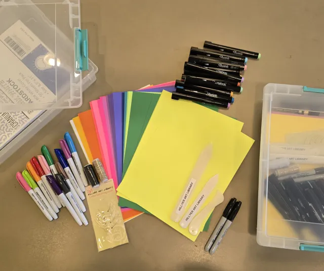 Zine kit featuring brightly colored cardstock, paint markers, three bone folders, sharpies, colored markers, and thread binding needles