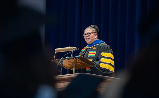 Sarah Willie-LeBreton in academic regalia, speaking at the School for Social Work commencement ceremony.