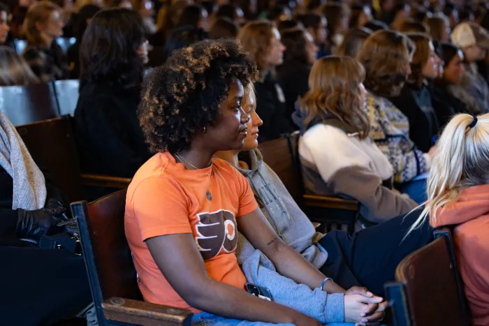 Two students sit in an auditorium holding hands.