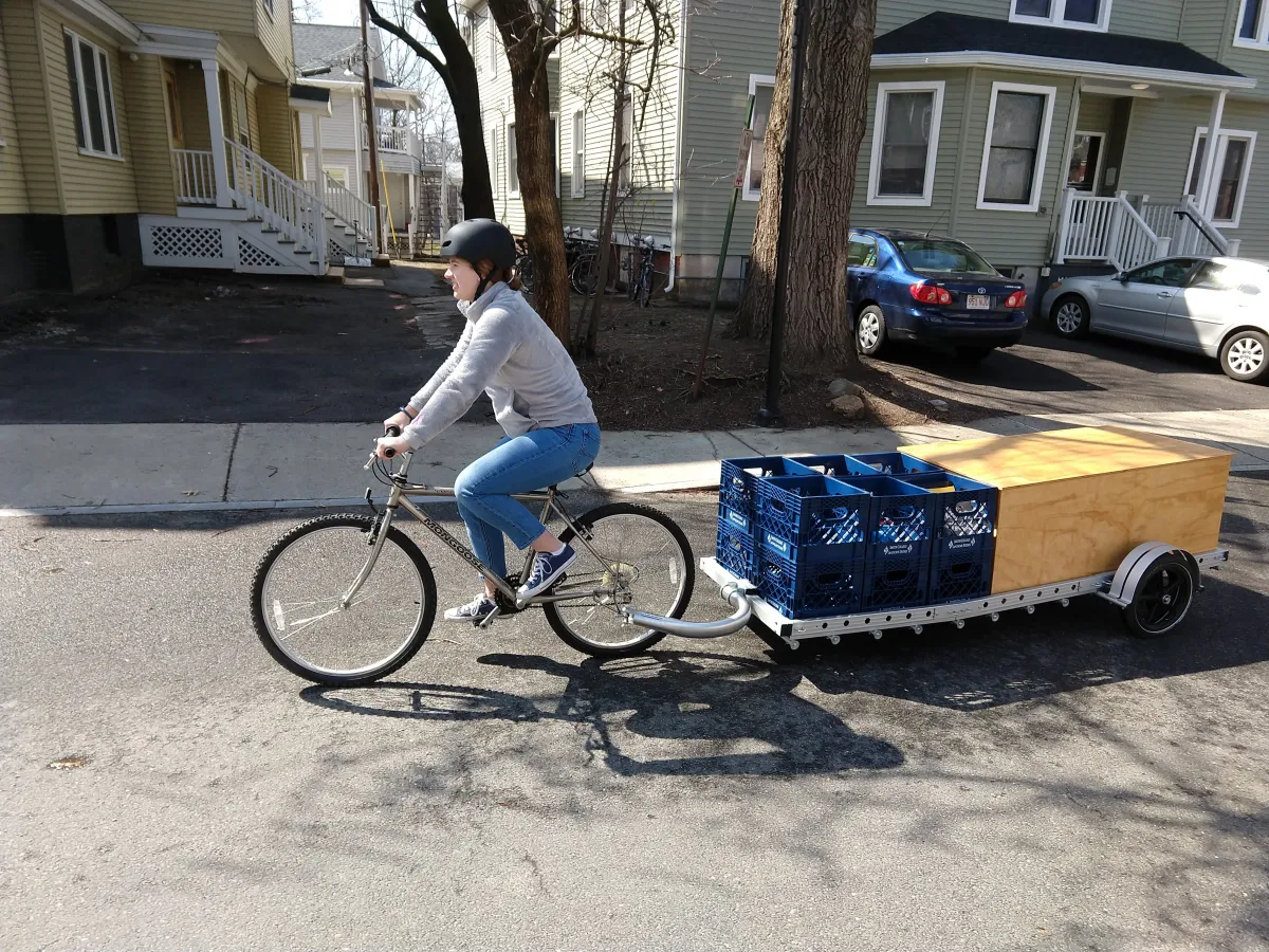 A student pedals a bicycle, pulling the portable ParkKit in tow