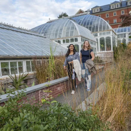 Two students walking in front of the Lyman Conservatory, smiling.