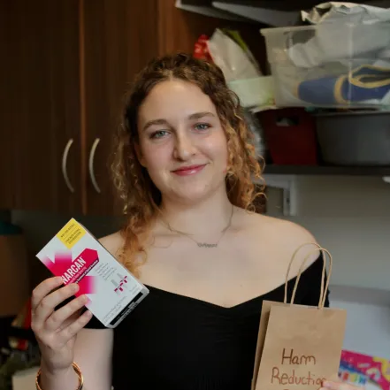 Cailin Young ‘24 prepares a harm reduction bag in the Schacht Center, holding up Narcan and smiling