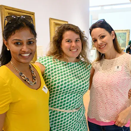 Three alumnae standing close together and smiling in the Smith College Museum of Art